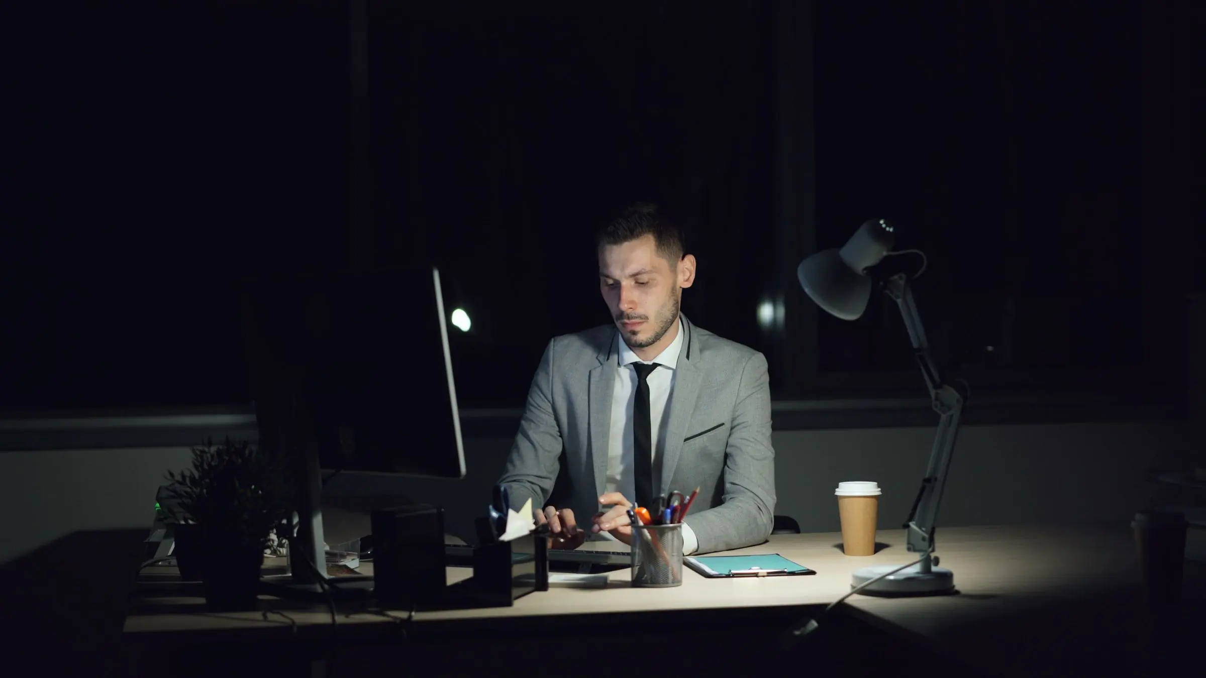 A desk at night, lit by a monitor, with a notebook of handwritten figures.