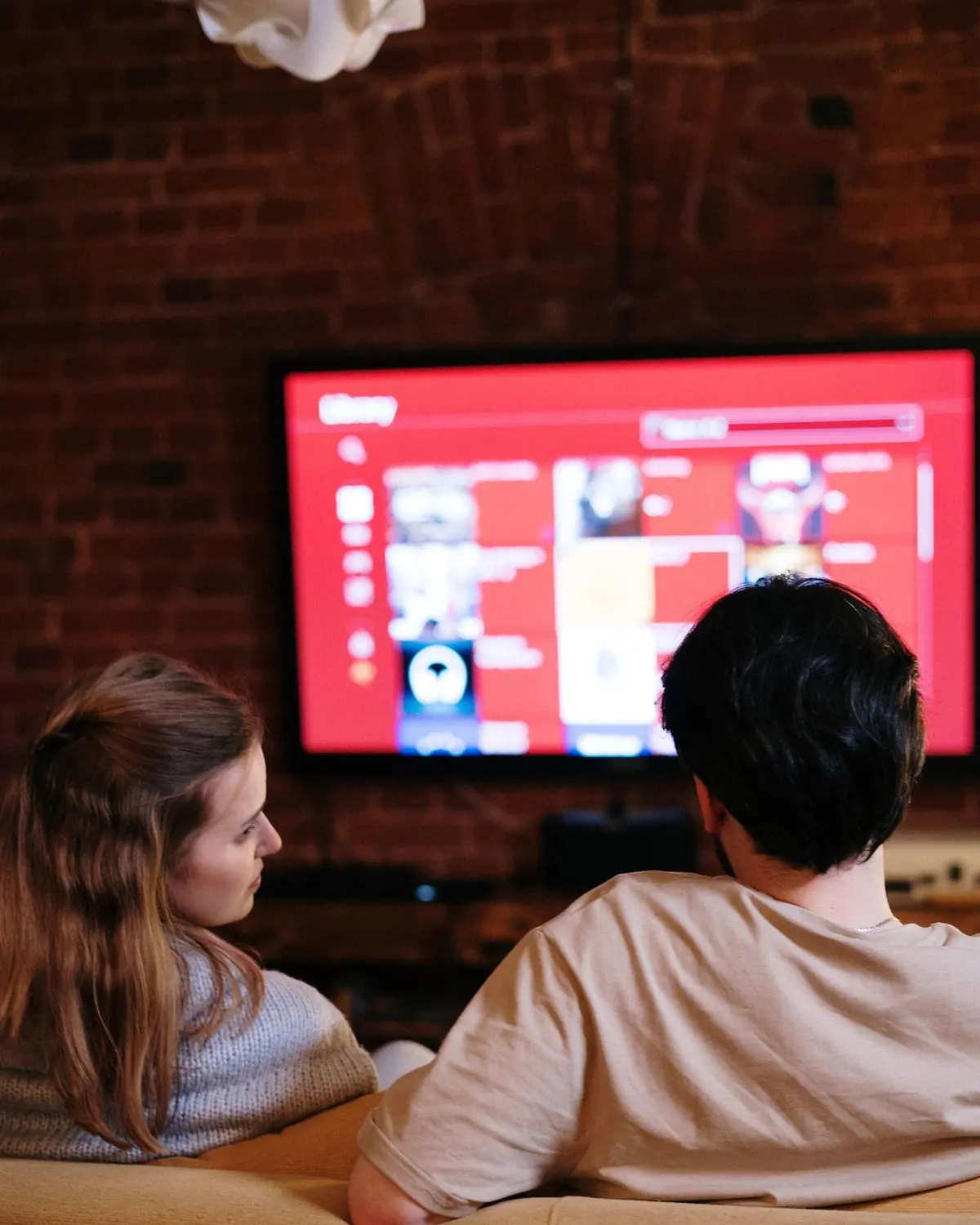 Two people on a couch watching a television in a dim living room.